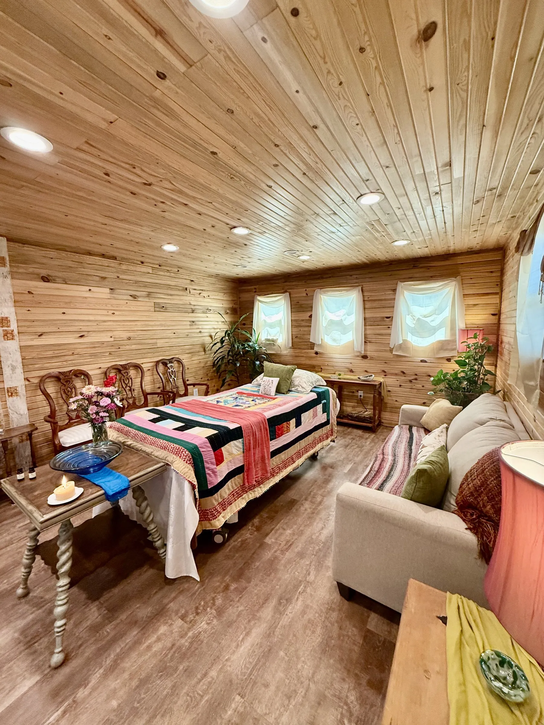 The laying-in room at our Lafayette funeral home: a bed dressed in a bright patchwork quilt, wood-panelled walls, soft window light, and an altar table with a candle and fresh flowers