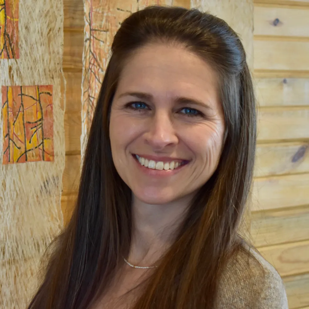 Nicole Matarazzo with long dark hair, smiling softly, against a warm wood-slat wall.